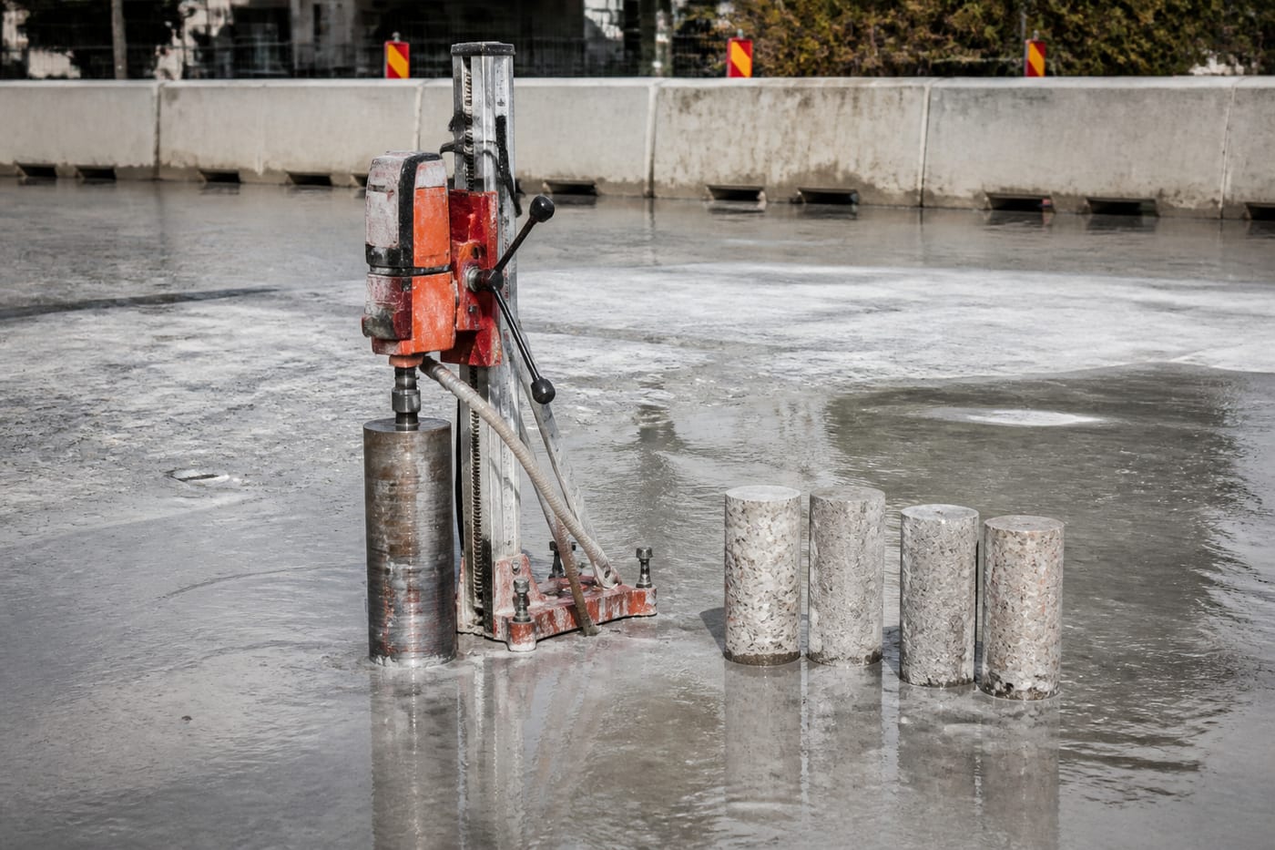 Diamond core drill on a wet concrete slab with cut concrete cores nearby